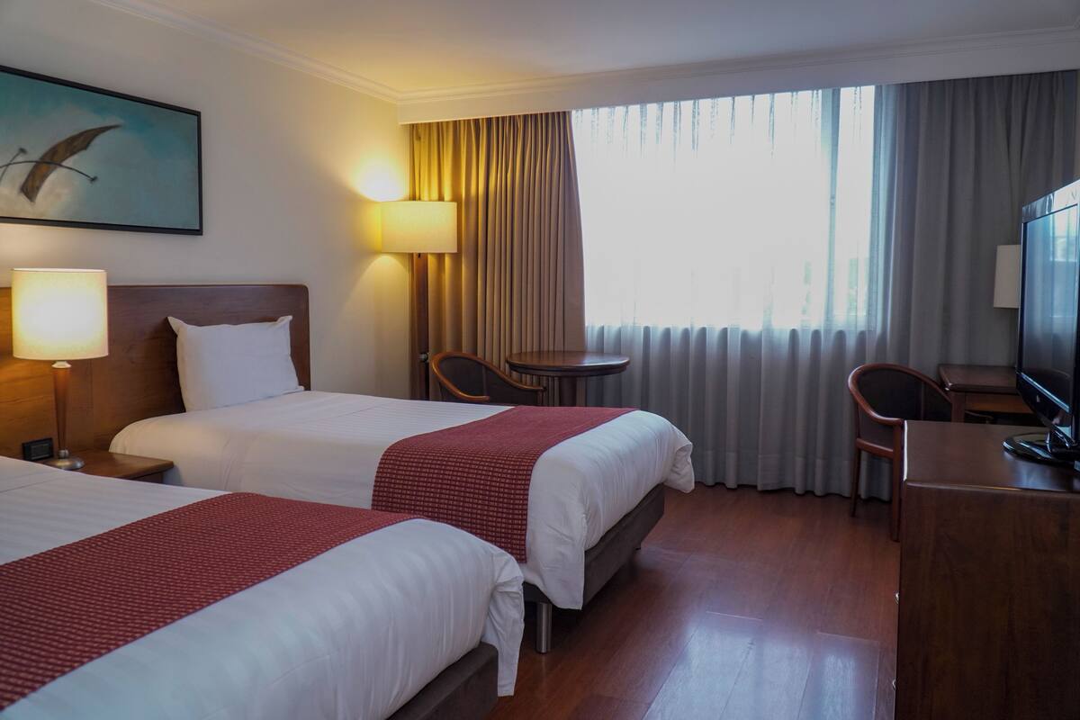 Une chambre d’hôtel avec deux lits, un bureau, une chaise, une lampe et un téléviseur.