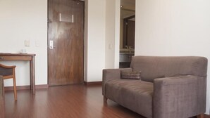 Una habitación con piso de madera, un sofá marrón, una mesita de madera y una puerta.