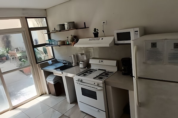 A kitchen with a gas stove, oven, microwave, and refrigerator. There are shelves above the counter with various items. - LA CASA DE LOS RIVAS (Tepic)