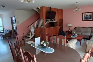 A dining area with a wooden table and chairs, a staircase, a sofa, and a lamp.