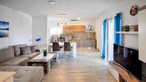 A modern living room with a sofa, coffee table, and TV. There is a dining area with chairs and a table, and a kitchen with cabinets and appliances. - Amazing apartment in Novigrad with swimming pool (Novigrad)