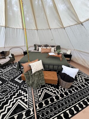 Ein Zeltinnenraum mit einem Bett, Kissen, einem kleinen Tisch und einem Stuhl.