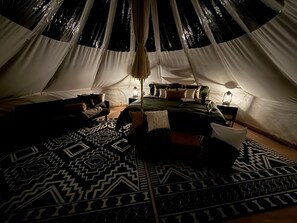 A tent with a bed, pillows, a rug, and two lanterns.