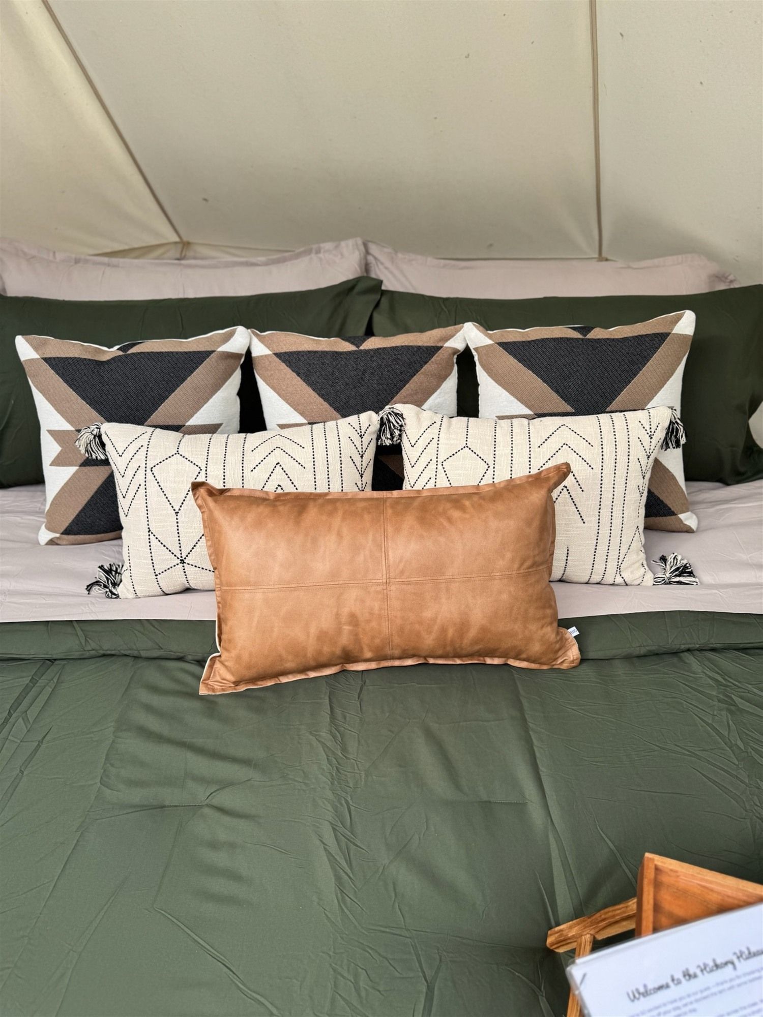 A bed with a green bedspread, multiple pillows with geometric patterns, and a brown pillow.
