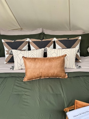 Un lit avec une couvre-lit verte, plusieurs oreillers aux motifs géométriques et un oreiller marron.