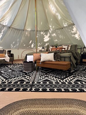 A tent interior with a sofa, pillows, a patterned rug, and a lamp.