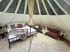 A tent interior with a bed, a sofa, a small table, and a rug.