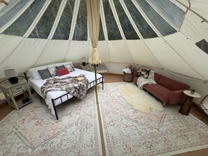 A tent with a bed, a sofa, a lamp, a rug, and a small table.