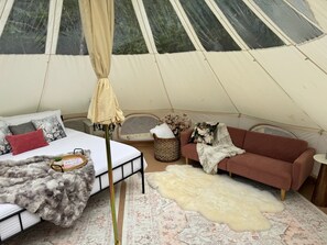 Interno di una tenda con un letto, un divano, una pelliccia e un cesto di vimini.