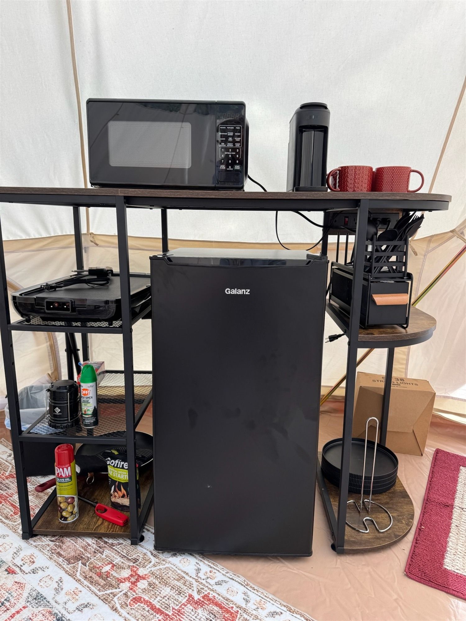 Ett litet, praktiskt kök med ett svart Galanz-kylskåp, en mikrovågsugn och en kaffebryggare placerad på ett metallstativ.