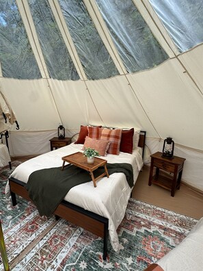 A tented accommodation with a bed, bedside tables, and a small table with a plant.
