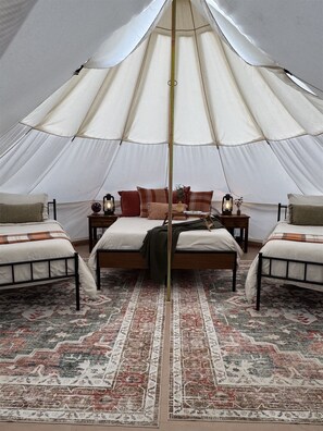 A tent with a bed and two chairs, a rug, and lanterns.
