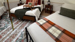 Alojamiento en tienda de campaña con cama, mesitas de noche y lámpara.