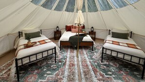Una carpa con tres camas, una cama central con dosel y una alfombra estampada.