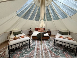 Una carpa con tres camas, una cama central con dosel y una alfombra estampada.