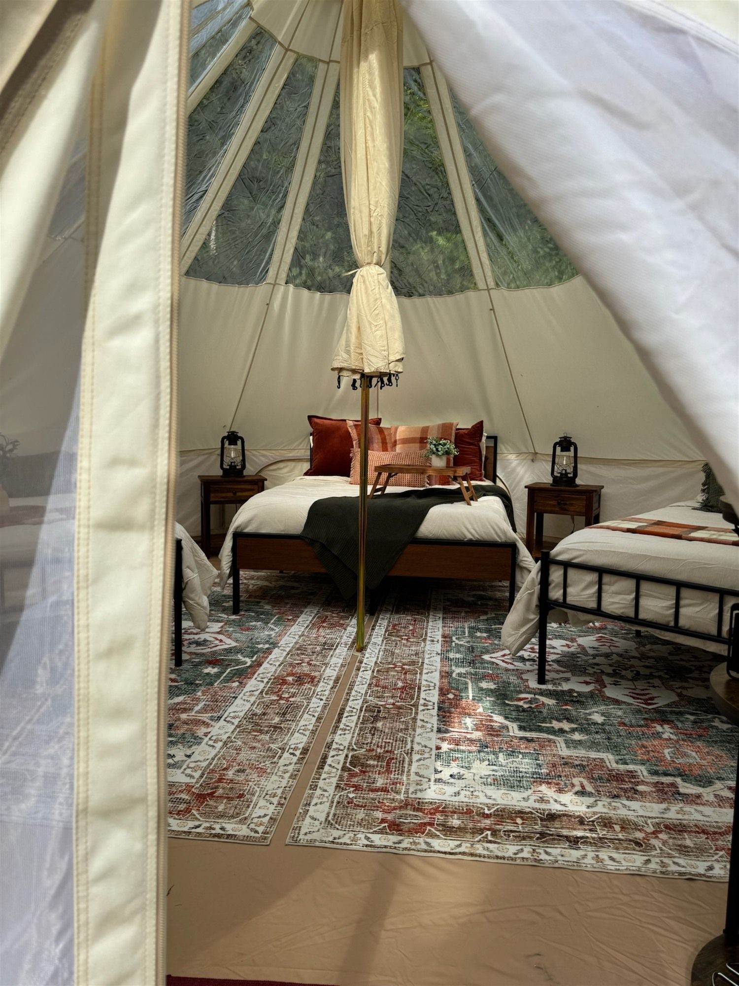 A tent with a bed, two bedside tables, a lantern, and a patterned rug.