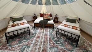 Una tienda de campaña con tres camas dispuestas en forma de U, una cama central con dosel y una alfombra estampada en el suelo.