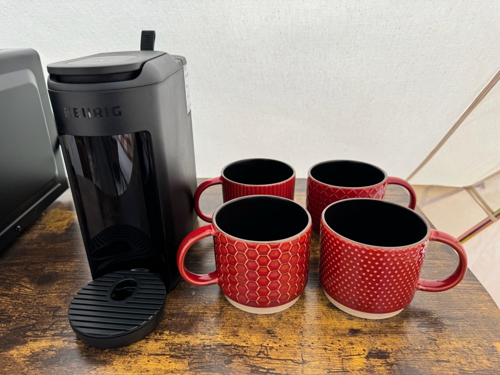 Een Keurig koffiezetapparaat met vier rode mokken op een houten oppervlak.