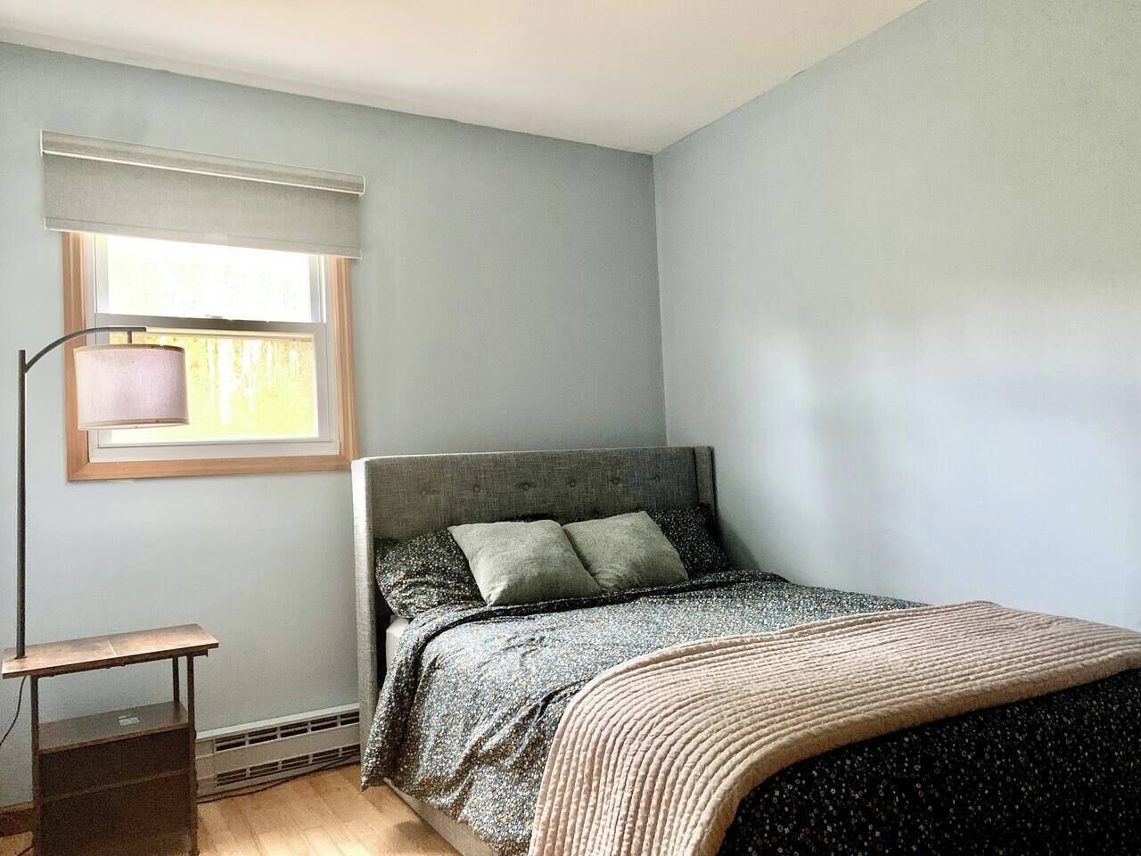 A bedroom with a bed, a nightstand, a lamp, and a window with blinds.