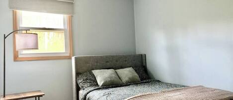 A bedroom with a bed, a nightstand, a lamp, and a window with blinds.