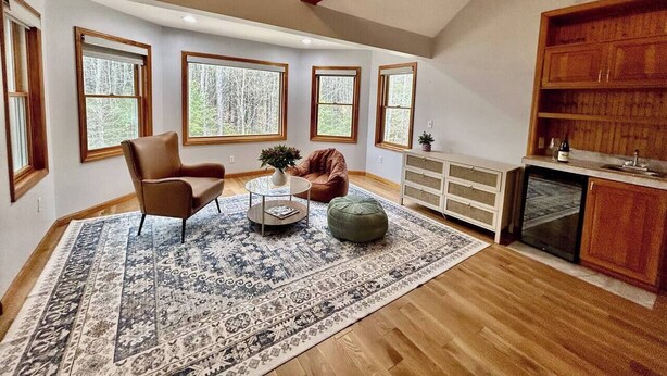 Une pièce de style « loft », dotée d’une grande fenêtre, d’un fauteuil en cuir marron, d’une table basse ronde, d’un pouf vert et d’une bibliothèque intégrée en bois.