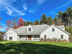 A two-story white house with a porch, a small front yard, and a clear blue sky.