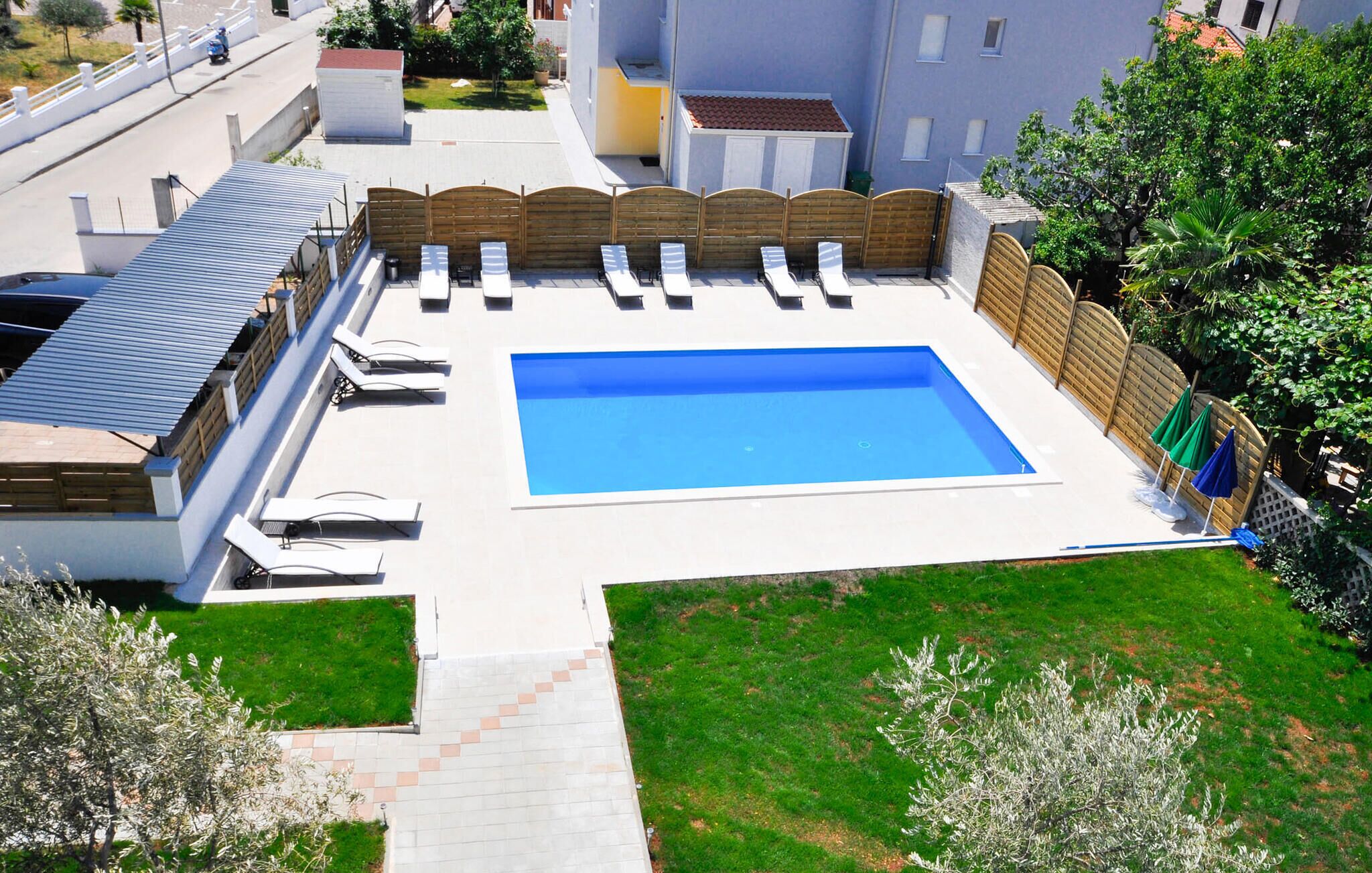 A rectangular swimming pool with a wooden fence and lounge chairs, surrounded by a well-maintained lawn and a building with a tiled roof.