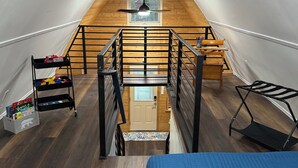 A high-ceilinged attic room with a wooden floor, a bed, a desk, and a chair.