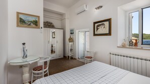 Un dormitorio con cama, cómoda, silla, una mesita y ventana con vistas.