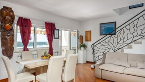 A dining area with a wooden table and chairs, a sofa, a staircase with a leaf-patterned railing, and a view of the sea through the windows. - Pet friendly apartment in Kampor with WiFi (Kampor)