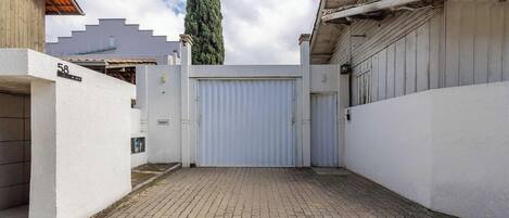 A gated courtyard with a paved walkway, a large white gate, and a building with a grey facade.