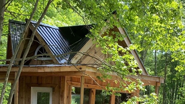 A rustic cabin with a wooden porch, a fire pit, and a car parked nearby.