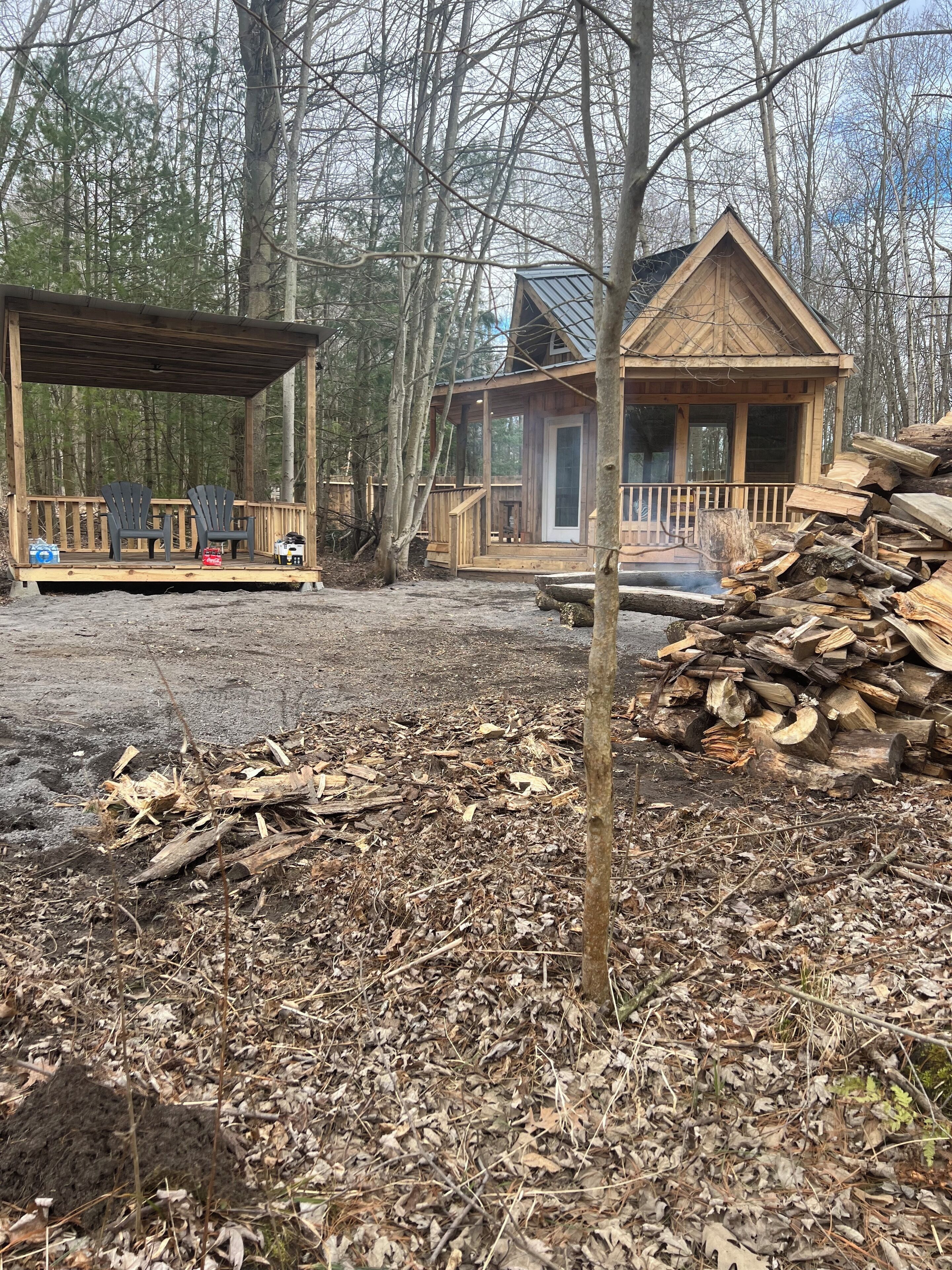 Une cabane dotée d’une terrasse en bois, de deux fauteuils Adirondack et d’un foyer.