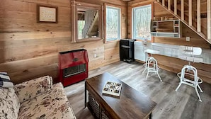 A cabin interior with a wooden interior, a red stove, a wooden table, and a staircase.