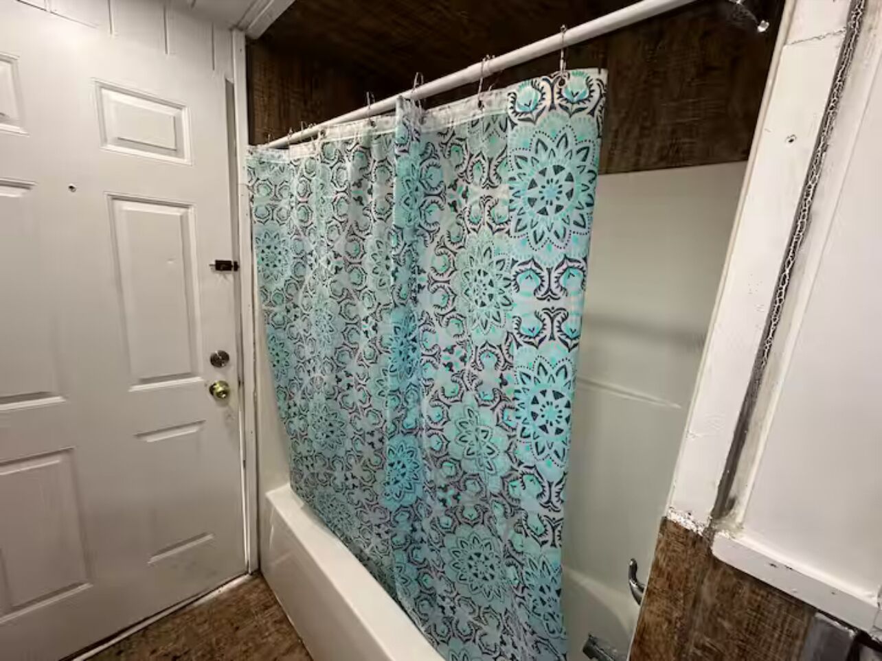 Une salle de bain avec un rideau de douche orné d’un motif géométrique, une porte blanche et un plancher en bois.