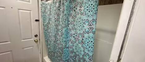 Une salle de bain avec un rideau de douche orné d’un motif géométrique, une porte blanche et un plancher en bois.