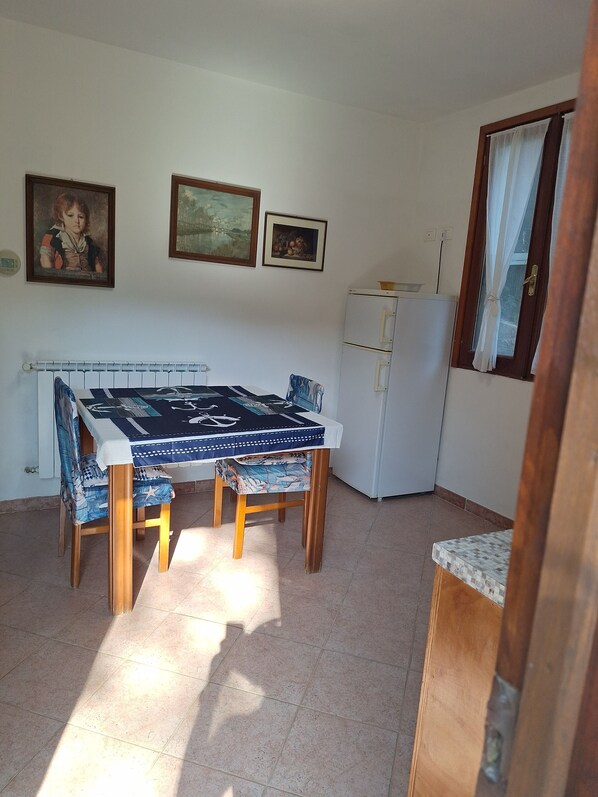 Un comedor con mesa y sillas, un refrigerador, y dos cuadros en la pared.