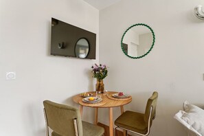 Un coin repas avec une table ronde en bois, deux chaises, un vase de fleurs et un miroir au mur.