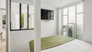 A bedroom with a bed, a TV mounted on the wall, and a sliding door to a balcony. - Lavie Maison AC & Terrace (Paris)