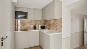 A compact kitchen with white cabinetry, a built-in oven, a sink, and a marble backsplash. - Lavie Maison AC & Terrace (Paris)
