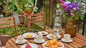 A wooden table set with plates of food, including croissants and a raspberry tart, cups of coffee, and a vase of flowers. - Lavie Maison AC & Terrace (Paris)