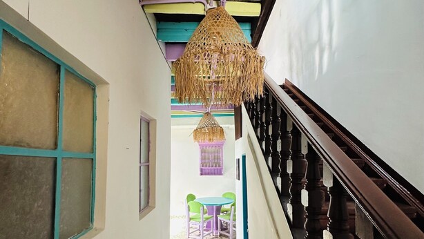 A narrow hallway with patterned floor tiles, a staircase with a wooden railing, and a hanging wicker lamp. - AQUI ME QUEDO here I stay (Bogota)