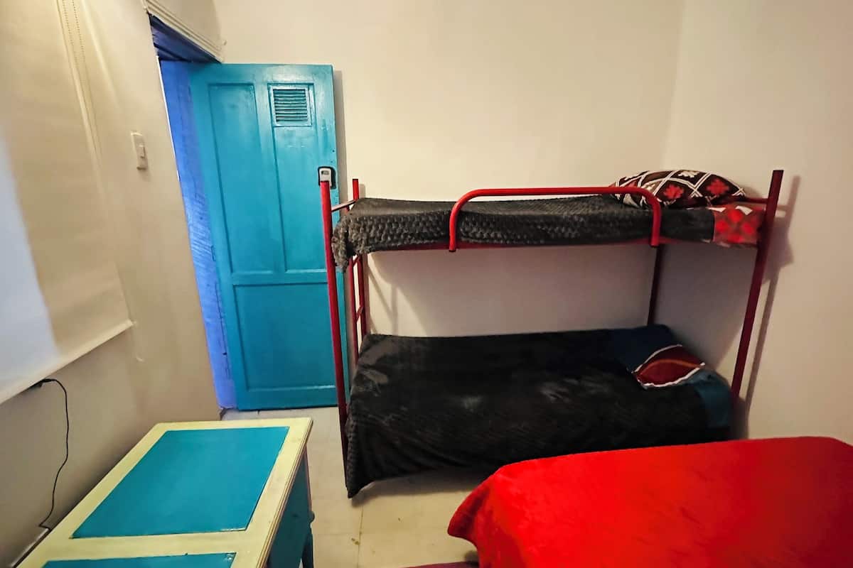 Ein Stockbett mit rotem Gestell, einer blauen Tür und einem kleinen Tisch mit blauer Tischplatte.