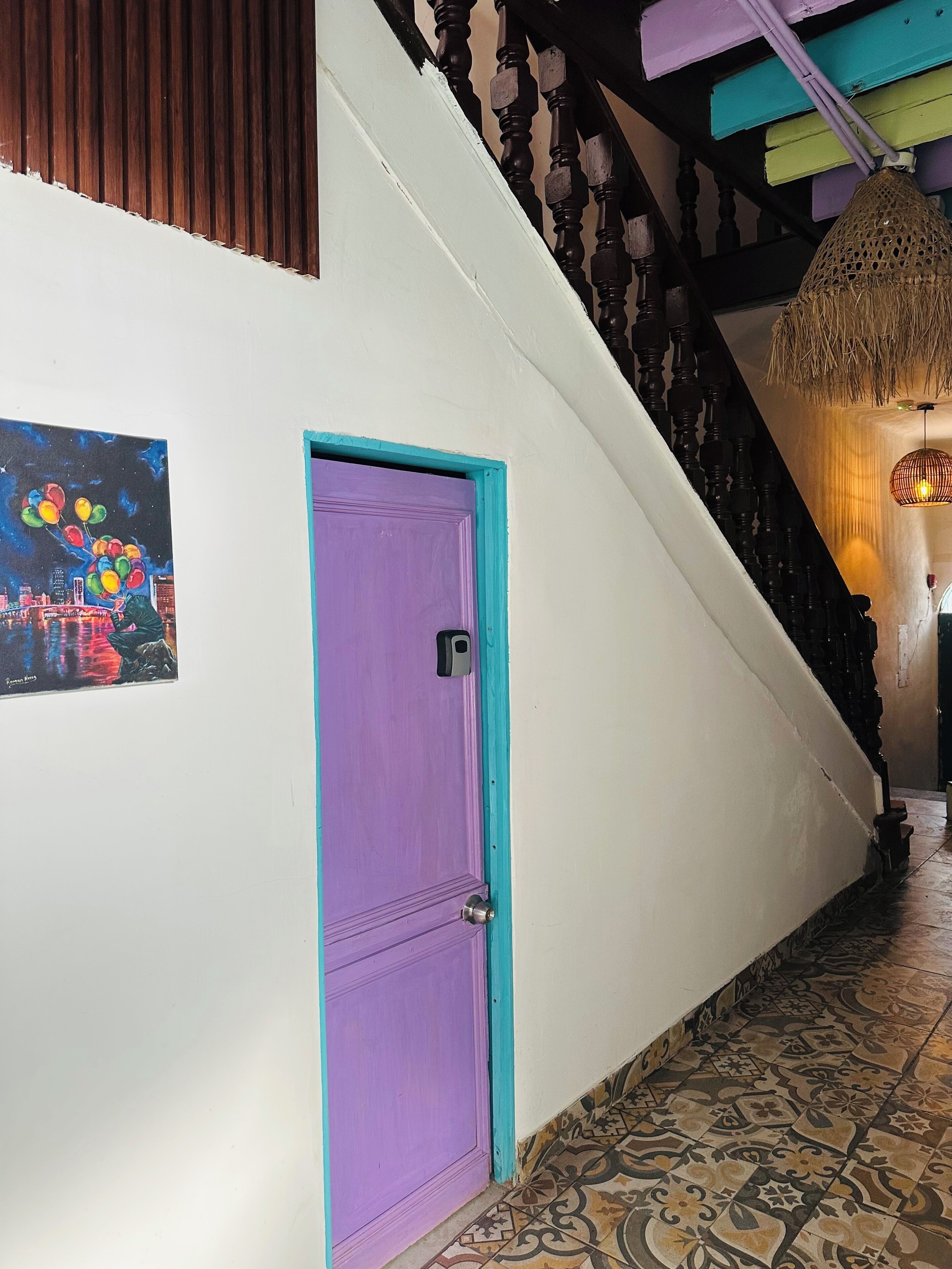 A staircase with a purple door, a hanging light fixture, and a cityscape painting on the wall.