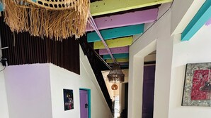 A narrow hallway with colorful walls and patterned floor tiles, leading to a staircase and a room with a table and chairs. - AQUI ME QUEDO here I stay (Bogota)