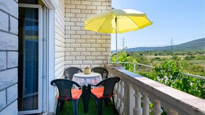 Een balkon met een tafel en stoelen, een gele parasol, en uitzicht op een wijngaard en heuvels.