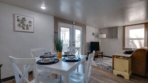 A dining area with a white table set for four, a sofa, a TV, and a small cabinet. - Dock&Volleyball! Near Downtown- Orange Oasis (Savannah)