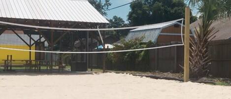 Un terrain de volleyball de plage avec une structure de toit en métal et des tables de pique-nique.