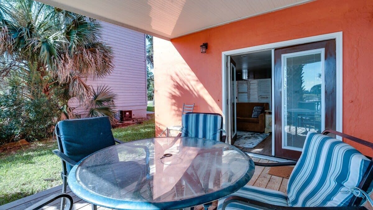 A glass-top table with chairs, a sliding glass door, and a palm tree in the background.