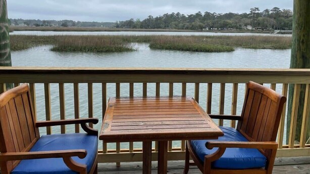 A wooden deck with a table and two chairs, overlooking a body of water with marsh vegetation. - Dock&Volleyball! Near Downtown- Orange Oasis (Savannah)